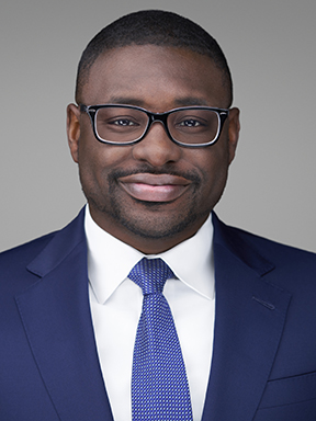 A man with glasses in a blue suit wearing a white dress shirt and a blue necktie.
