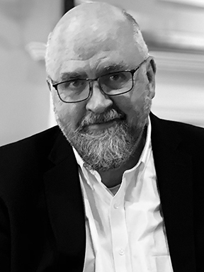 A bearded man in a tie seated at a desk in a professional office environment.