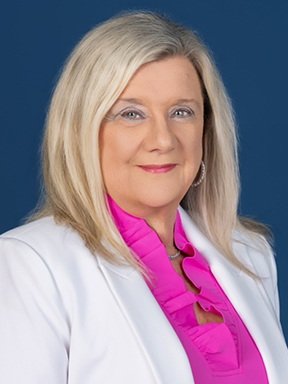 A blond woman in a white blazer and a pink blouse.