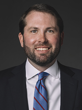 A young man dressed in a suit and tie smiling warmly.
