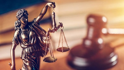 Bronze Lady Justice statue in front of an out-of-focus gavel and sounding block.
