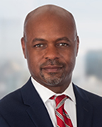 A man in a navy blue suit with a white dress shirt wearing a red and gray striped necktie.